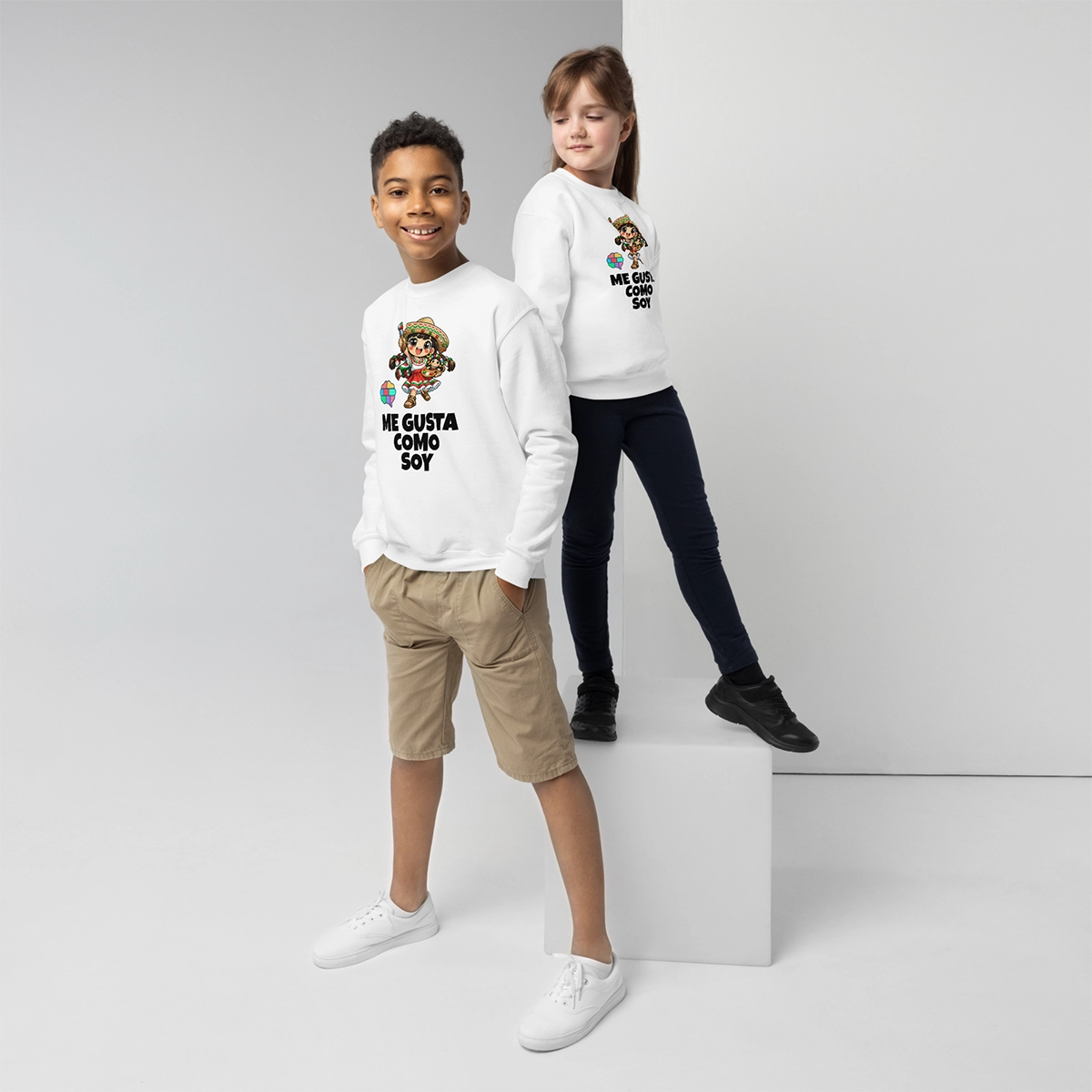 Niño y niña posando con la sudadera técnica de Frida Emociones en color blanco roto, mostrando el lema de autoaceptación "Me gusta como soy"